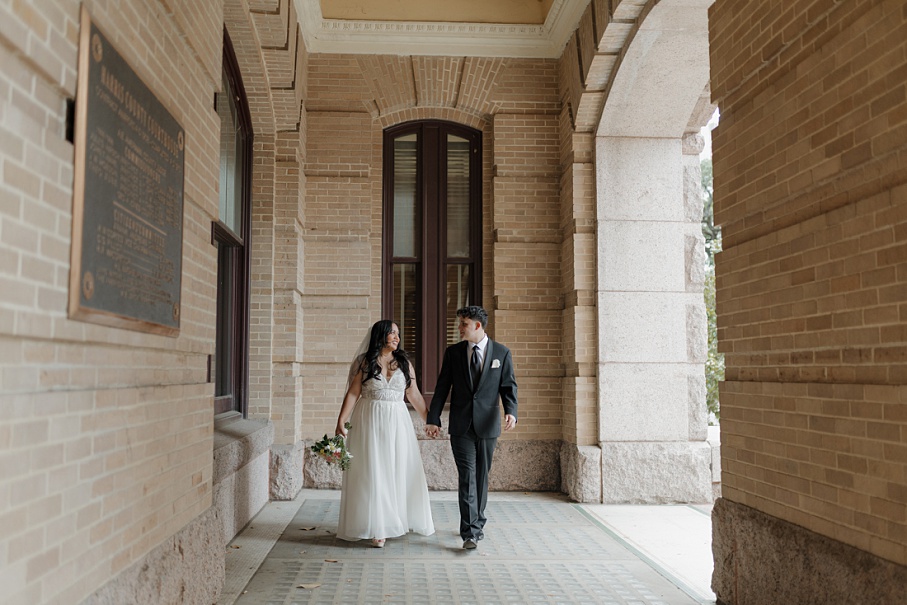 Newlyweds walking hand in hand outside the 1910 courthouse, captured by Houston elopement photographer