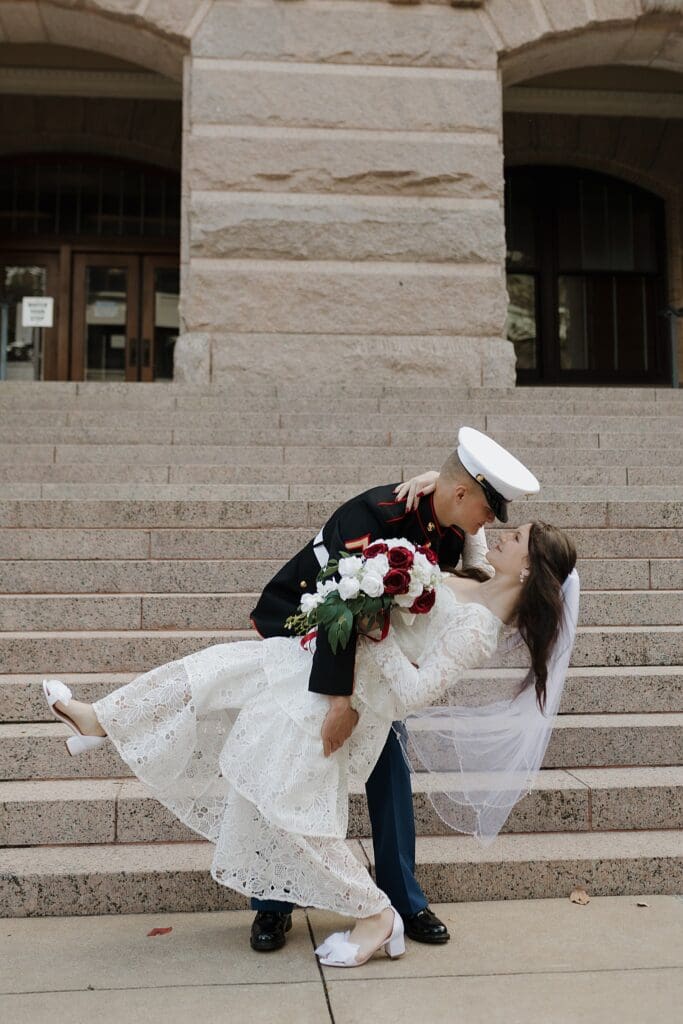groom in military uniform dipping his bride outside the 1910 historic courthouse 